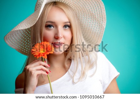 gorgeous blond model wearing hat and white T-shirt with gerbera looking at the camera. sunny woman