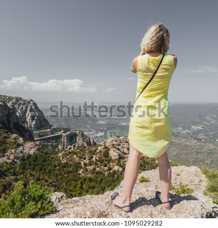 Female traveler enjoying the views from the mountains of Montserrat in Spain and makes a photo on her camera. The girl in a yellow dress on background of the nature