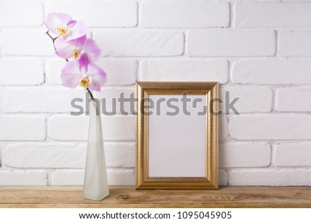 Gold decorated frame mockup with tender pink orchid in the elegant glass vase. Empty frame mock up for presentation artwork. Template framing for modern art.