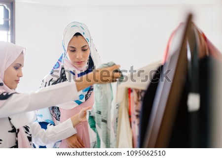 Two Muslim women in head scarves (tudung) are having a discussion while looking over some fabric. 
