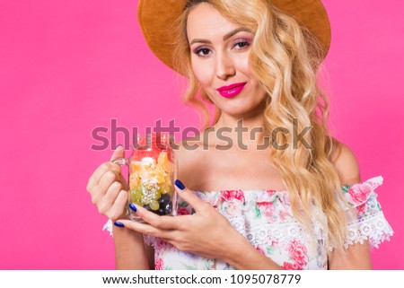 Portrait of young woman holding tasty fresh fruit in bottle on pink background
