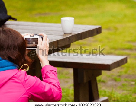 Tourist adult woman taking picture using professional camera. Photographing mug on bench outdoor.