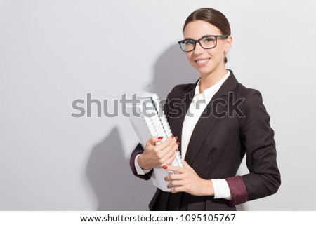 Young smiling businesswoman in glasses holding books in her hands. Fashion style photoshoot with har light source
