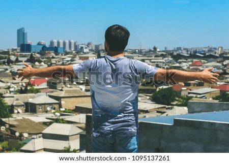 The young man with open hands on a roof looks on the city.
