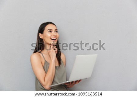 Portrait of a happy asian woman using laptop computer and looking away isolated over gray background