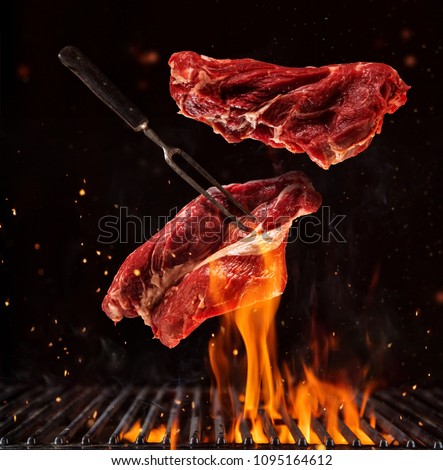 Flying pieces of beef steaks above grill grid, isolated on black background. Concept of flying food, very high resolution image