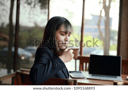 Asian business woman working in in coffee shop cafe with laptop paper work hand Holding coffee   (Business woman concept.)
