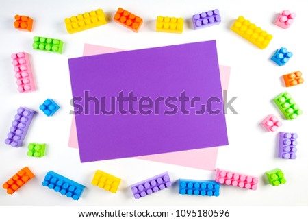 Colorful plastic construction blocks frame with violet blank card on white background