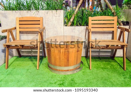A bucket shape wooden table and chair on artificial grass with nature hedge for home decoration or gardening.