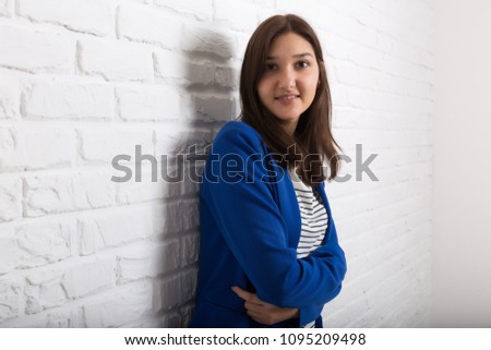 A young pretty smiling girl against a white loft-style brick wall. She looks at the viewer. Copy space.