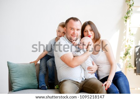 Photo of happy married couple with two young sons sitting on sofa