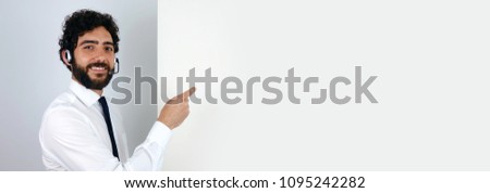 Handsome call center man with a smiling expression  holding a blank banner and pointing a copy space for your text or advertising, over a grey background