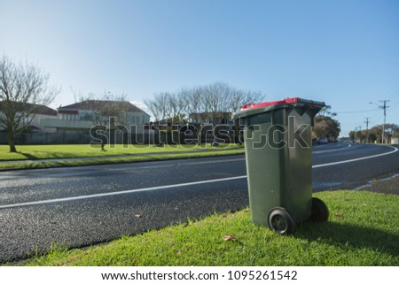 Trash Can with Red Lid on Street Side in front of House Royalty-Free Stock Photo #1095261542