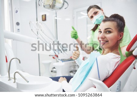 A young woman is satisfied with the work of the dentist and holds up her thumb.
