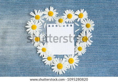 Beautiful Vintage Floral background with copy space. Frame in the shape of heart of chamomile flowers with Blank page notebook on blue denim background. Top view. Flat lay. Web banner