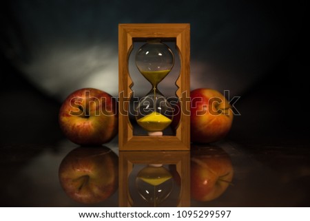 Hourglass. Red apples. Concept: time, youth, eternity.