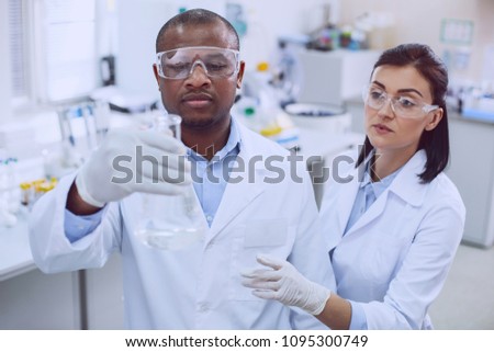 Team spirit. Determined afro-american biologist conducting a test and his colleague helping him