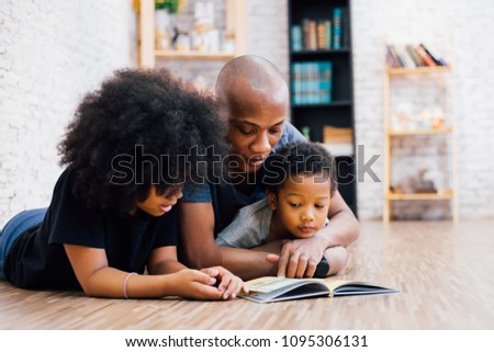 African American father reading a fairy tale fable story for kids at home. Happy family lying on the floor indoors Royalty-Free Stock Photo #1095306131
