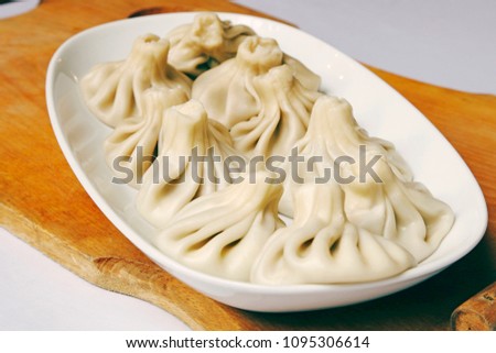 Hot portion of Khinkali (Georgian dumplings) served on a white plate and wooden board