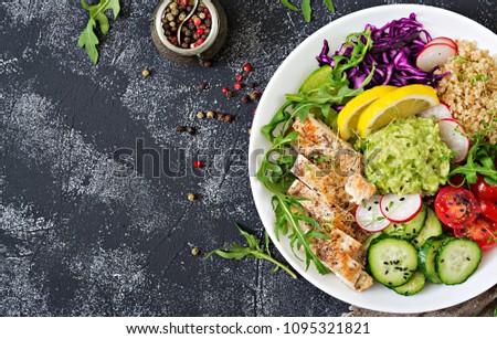 Healthy dinner. Buddha bowl lunch with grilled chicken and quinoa, tomato, guacamole, red cabbage, cucumber and arugula on gray background. Flat lay. Top view