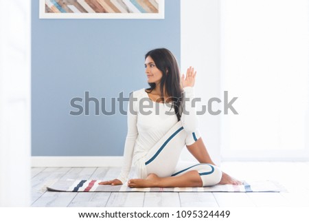 Charming young woman in a gymnastic suit doing yoga exercises Marichiçana sitting on a rug in wooden floor in a gym