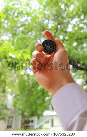 A hand in white shirt holding a compass, just meaning the new way to successful business. Keep walking. Soft focus with blurred green leaves and building background. Business concept.