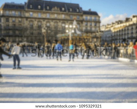 Blurry background texture. Crowds of people having fun at outdoor winter skating rink surrounded by historic architecture. Paris, France.