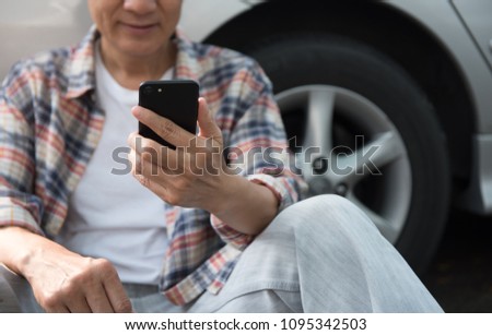 Happy young asian man, hipster sitting on the ground outside a car and using mobile smart phone, videocalling with his friend. Summer holiday, weekend travel concept. Close up Royalty-Free Stock Photo #1095342503