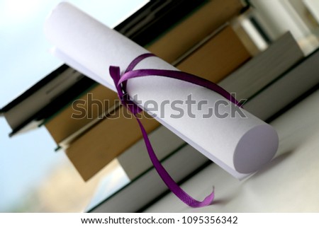 Graduation scroll, tied with violet ribbon and books. Royalty-Free Stock Photo #1095356342