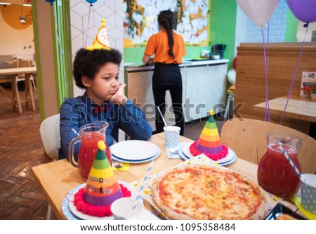 Funny mixed cute boy get bored on the kids birthday party. Children mood on holidays. Happy birthday boy