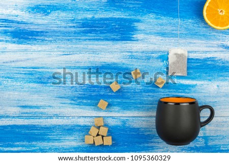 The Cup of tea on a blue background. Tea bag and sugar and orange slices. Summer