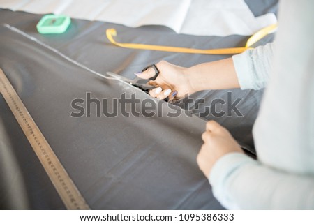 High angle close up of unrecognizable female tailor cutting fabric with scissors while sewing custom made clothes, copy space