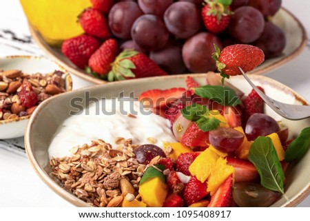 Fruit berry salad with yogurt and granola for healthy breakfast on dessert. Plate with grape, strawberry, mango and orange