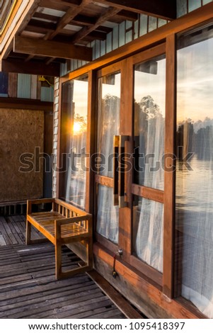 Wooden chair in front of hotel room with reflected of sunset sea view