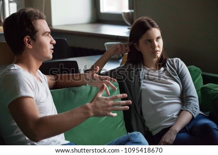 Annoyed girl tired of listening to boring boyfriend sitting on sofa at home, bored woman not interested in tedious monologue of talkative nerd friend or husband disbelieving dull story concept Royalty-Free Stock Photo #1095418670