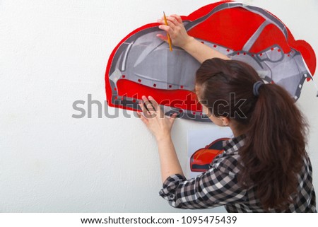 A close-up of a female artist draws a picture of a car and draws it in red on a white wall in the children's room