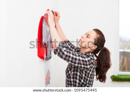 A close-up of a female artist draws a picture of a car and draws it in red on a white wall in the children's room
