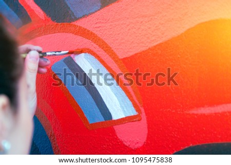 Close-up of a female artist in black and white shirt draws a red car on a wall with a pencil on a white wall in a children's room