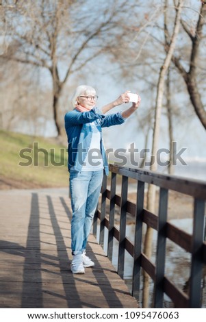 My hobby. Joyful old woman taking pictures while walking in the park
