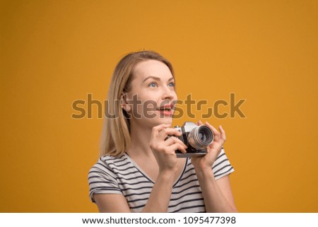 Cheerful hipster girl with retro camera on a yellow background