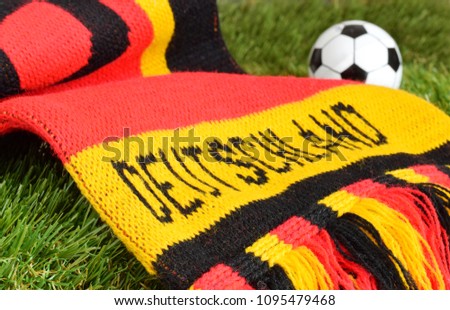 German scarf in red black gold rolled up  with text in german language "Germany" is on football field.