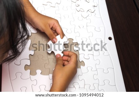 a little girl put the pieces of jigsaw puzzle to complete the mission. 