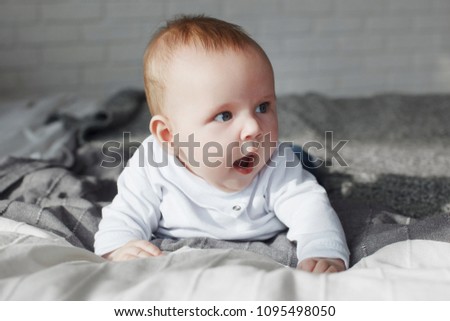 Happy blond infant with blue eyes in bed sports and smiling