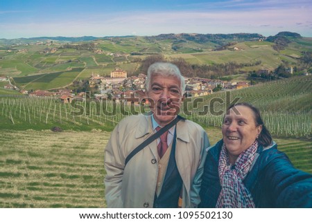 Senior couple take selfie in the small town of Barolo among hills and green vineyards in Piedmont, Northern Italy.