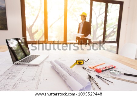 Close-up blueprints, laptop and engineer on working desk with blurred background or engineer architect standing near to a window.