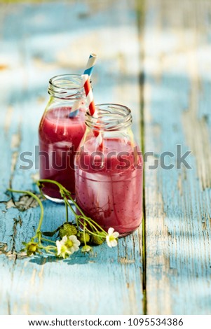 Bright, vibrant strawberry smoothies in glass jars on a rustic outdoor summer picnic table setting.
