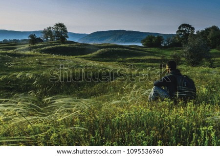 Man sitting in the meadow and enjoying the view in the early morning