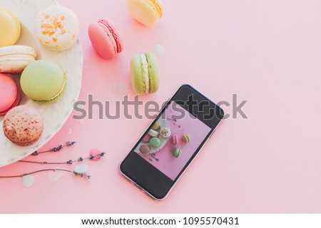 modern food photography concept. phone with photo of stylish colorful macaroons in vintage plate on trendy pink paper with lavender. space for text. instagram blogging concept