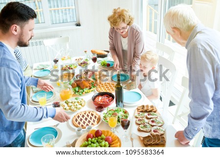 Portrait of happy two generation  family enjoying dinner together round festive table tending to kids and laughing during  holiday  celebration in modern sunlit apartment, copy space