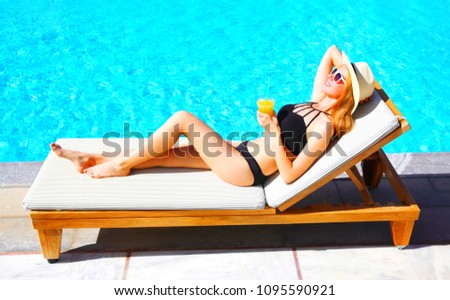 Summer holidays - happy young woman resting with juice from cup on deck chair, blue water pool background